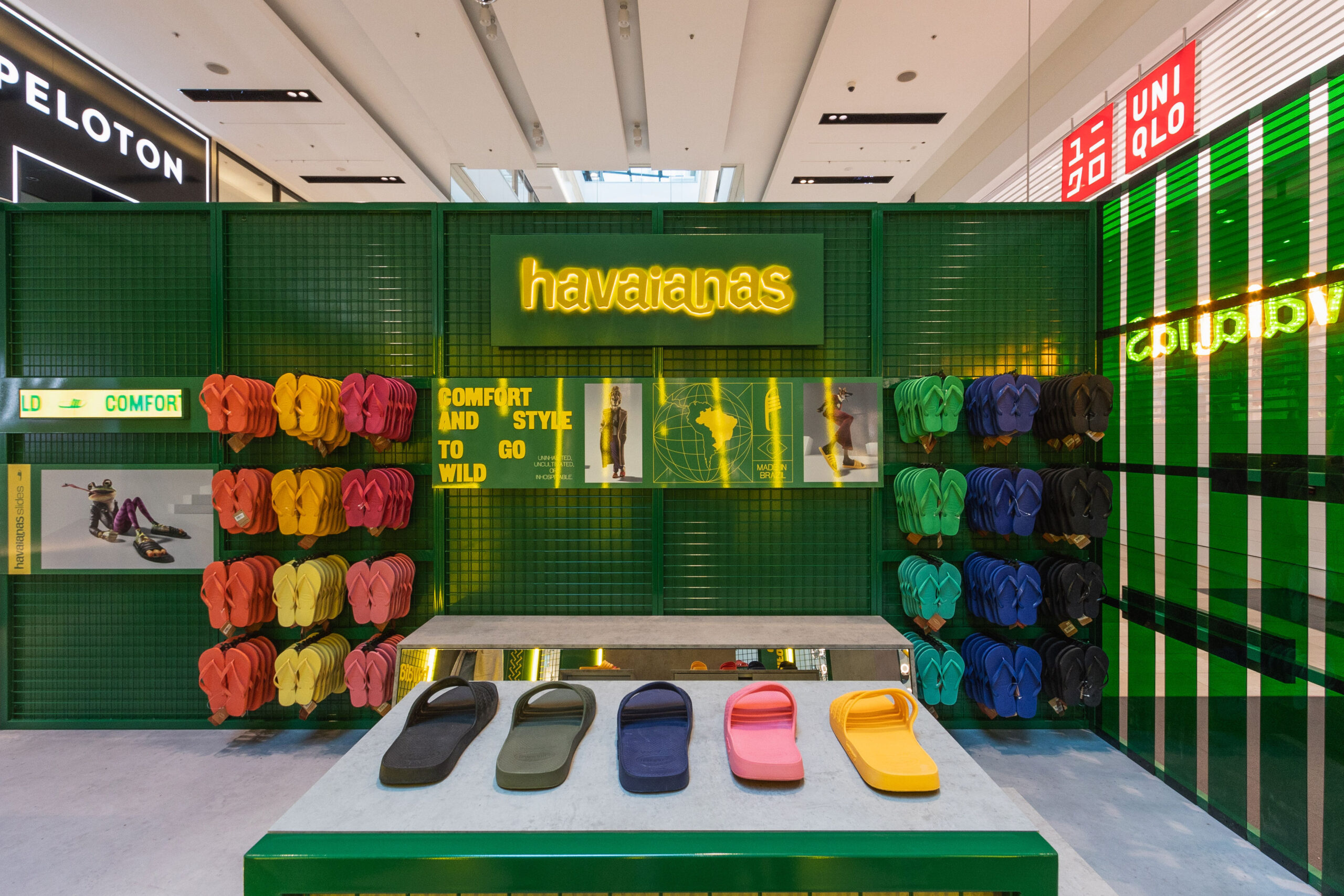 Pop-Up Brand Activation For Havaianas by Little and Large Events. Displayed on the back wall is a large yellow, backlit logo on a green mesh wall with displays of colourful slides on either side.