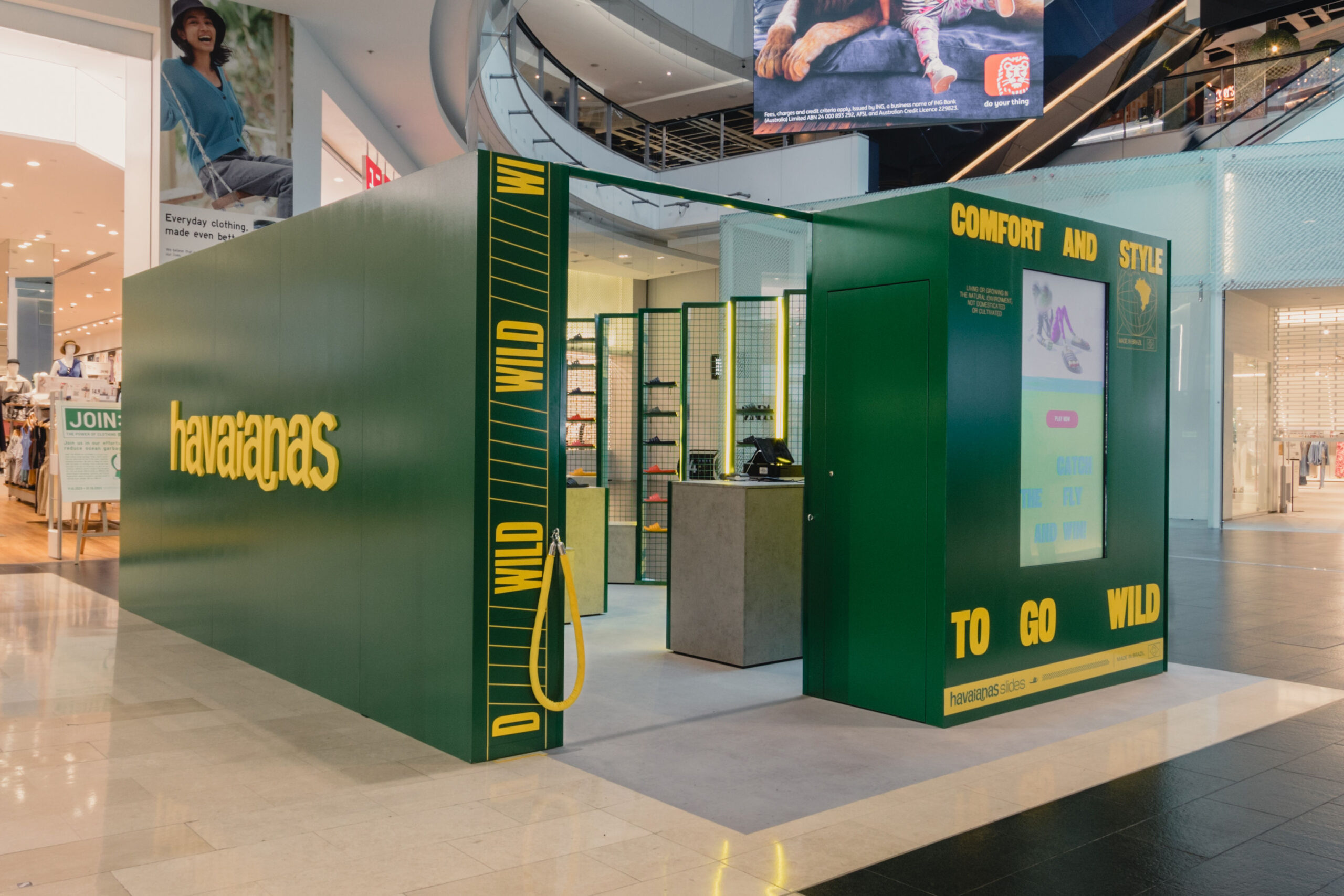 Angled View of Rear End Entrance to Pop-up Store. Green Display with Yellow Lettering of the Logo, Brand Messaging, and an Interactive Digital Display.